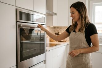 Femme ouvrant un four encastrable en inox intégré dans une cuisine moderne blanche avec meubles encastrés